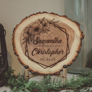 May include: A wooden slice with a geometric frame and floral design, engraved with the names Samantha and Christopher and the date 05.24.21.