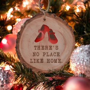 May include: A wooden Christmas ornament with a red ruby slipper design and the text "There's no place like home."