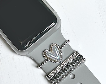 Pode incluir: Um Apple Watch cinza com um charme de coração prateado e uma banda de contas prateadas.