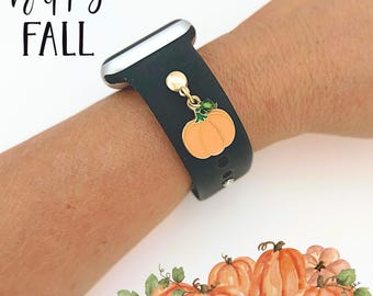 Puede incluir: Correa de reloj negra con un dije dorado con una calabaza naranja con hojas verdes. Las palabras "happy FALL" están escritas en escritura negra. Hay calabazas de acuarela en la parte inferior de la imagen.