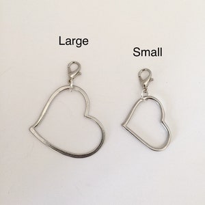 May include: Two silver heart-shaped charms with clasps. The charm on the left is labeled "Large" and the charm on the right is labeled "Small".