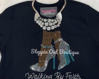 May include: Black t-shirt with a rhinestone design of two high heels and the text "Walking By Faith". The design also includes a rhinestone necklace.