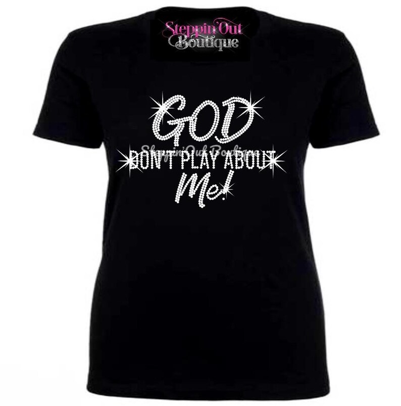 May include: Black t-shirt with the text "GOD DON'T PLAY ABOUT ME!" in a sparkling, rhinestone-like font. The shirt also features the text "Steppin Out Boutique" in a cursive font at the top.