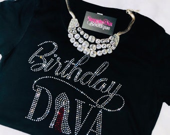 Puede incluir: Camiseta negra con pedrería que deletrea "Birthday Diva" y un zapato de tacón alto de pedrería roja. La camiseta tiene un collar plateado con pedrería transparente.