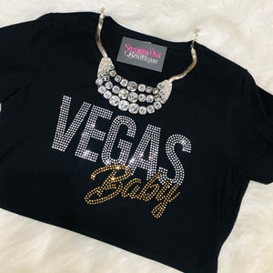 Pu&ograve; includere: Maglietta nera con scritta in strass "Vegas Baby" e una collana argentata a pi&ugrave; strati con un'etichetta "Stepping Out Boutique".