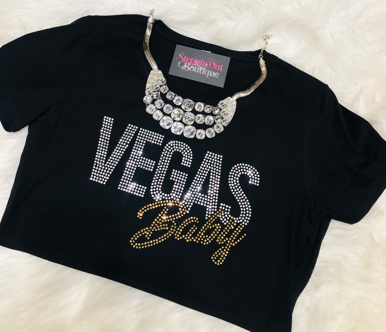 Pu&ograve; includere: Maglietta nera con scritta in strass "Vegas Baby" e una collana argentata a pi&ugrave; strati con un'etichetta "Stepping Out Boutique".