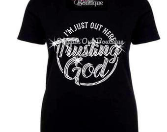 May include: Black t-shirt with the text "I'm just out here trusting God" in silver rhinestones.