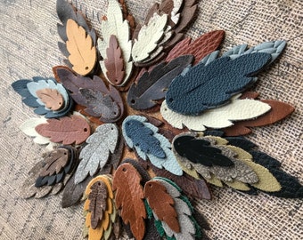May include: Assortment of leather leaf shapes in various colors, including brown, tan, gray, blue, and black. The leaves are arranged in a circular pattern on a textured fabric background.