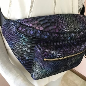 May include: A black fanny pack with a snakeskin pattern in shades of purple, blue, and green. The pack has a gold zipper and a black strap.