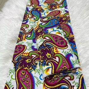 以下が含まれることがあります： 白地に紫、青、緑、黄、赤の色合いのペイズリー柄が施された布地。布地は半分に折り畳まれており、両側に柄が見えます。