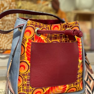 May include: A blue and red bucket bag with a geometric pattern. The bag has a long strap and a drawstring closure.