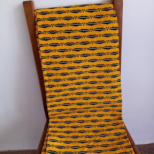 Peut inclure: Un tissu jaune avec un motif géométrique noir et blanc drapé sur une chaise en bois.