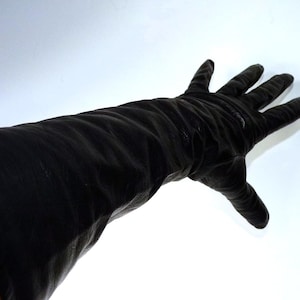May include: Black leather glove extending up the arm. The glove is a solid black color and appears to be made of a soft, supple leather. The fingers are extended, and the glove is reaching towards the viewer.