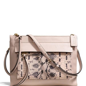 Puede incluir: Un bolso bandolera de cuero rosa claro con una solapa de estampado de piel de serpiente. El bolso tiene una cremallera dorada y una correa dorada.