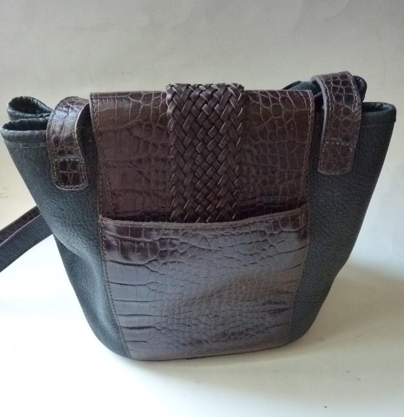 May include: A brown leather handbag with a black leather flap and a braided strap. The bag has a crocodile-embossed design.