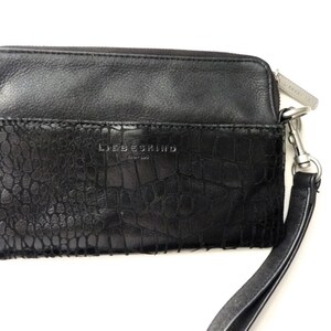 Könnte beinhalten: Schwarze Lederclutch mit Kroko-Prägung und silbernem Reißverschluss. Die Clutch hat einen abnehmbaren Riemen und der Markenname "Liebeskind Berlin" ist auf der Vorderseite geprägt.