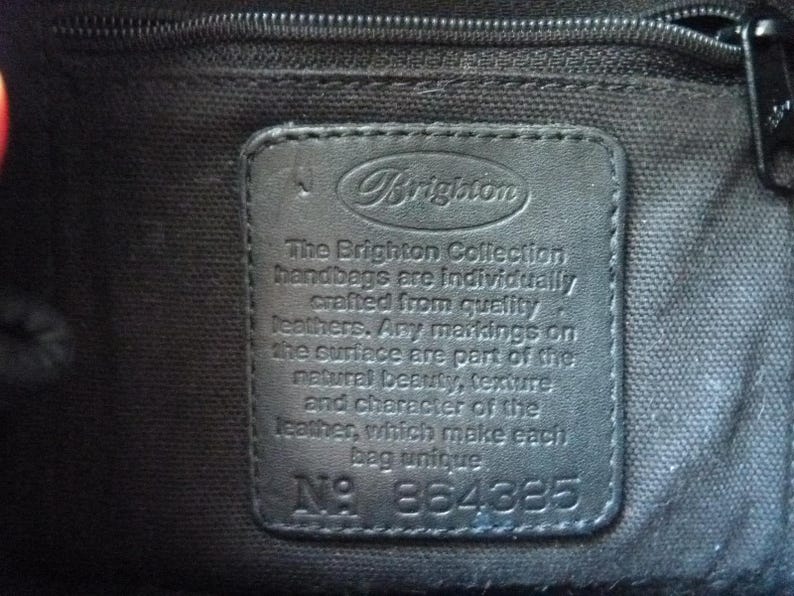 May include: A black leather tag with the text "Brigiton" and the words "The Brighton Collection handbags are individually crafted from quality leathers. Any markings on the surface are part of the natural beauty, texture and character of the leather, which make each bag unique" and the number "N&deg; 864885".