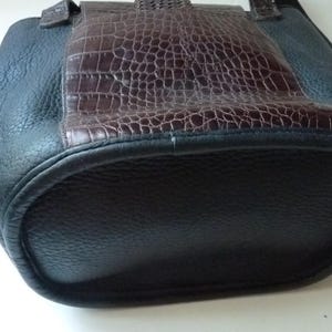May include: A black leather tote bag with a brown crocodile embossed leather panel on the front. The bag has a top handle and a zipper closure.