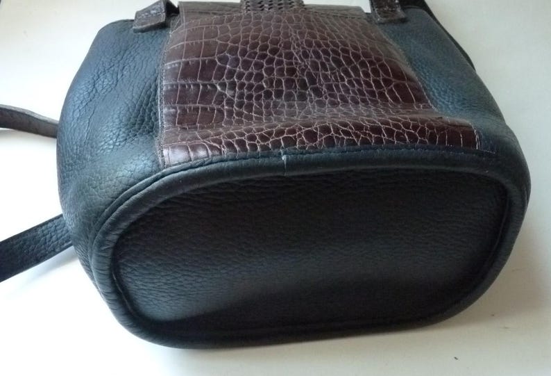 May include: A black leather tote bag with a brown crocodile embossed leather panel on the front. The bag has a top handle and a zipper closure.