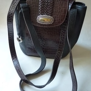 May include: A brown and black leather shoulder bag with a braided strap and a silver and gold buckle. The bag has a crocodile-embossed pattern.