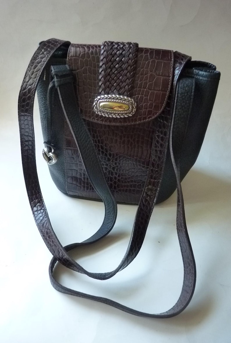 May include: A brown and black leather shoulder bag with a braided strap and a silver and gold buckle. The bag has a crocodile-embossed pattern.