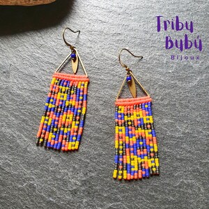 May include: A pair of long, colorful beaded earrings with a triangle-shaped brass pendant at the top. The beads are in shades of blue, yellow, orange, and black. The earrings are labeled "Triby Bubú Bijoux".