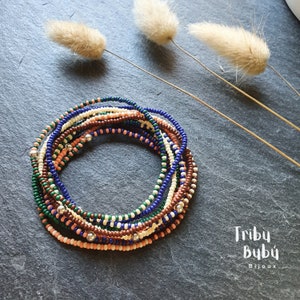 May include: A set of 10 colorful beaded bracelets in shades of peach, brown, cream, green, and blue. The bracelets are stacked on top of each other and feature silver beads. The text "Triby Bubu Bijoux" is visible in the bottom right corner of the image.