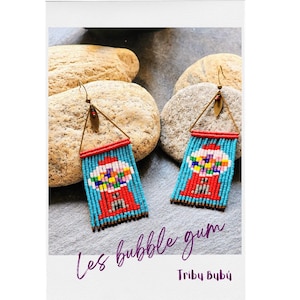 May include: A pair of beaded earrings featuring a gumball machine design with a red base and a light blue background. The earrings are suspended from a triangular gold-tone metal frame with a small leaf charm and include the text Les bubble gum.