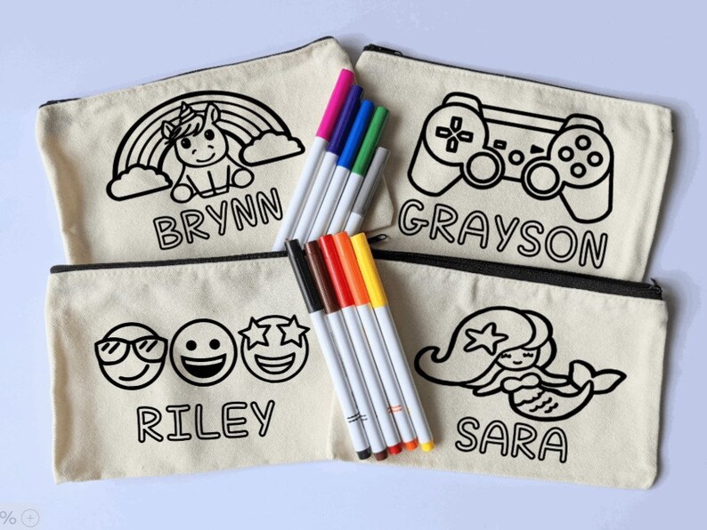 Puede incluir: Cuatro estuches de cremallera de lona con contornos negros de un unicornio, un mando de videojuegos, tres emojis y una sirena. Cada estuche tiene un nombre escrito debajo de la imagen: Brynn, Grayson, Riley y Sara. Los estuches van acompa&ntilde;ados de un juego de ocho rotuladores de colores.
