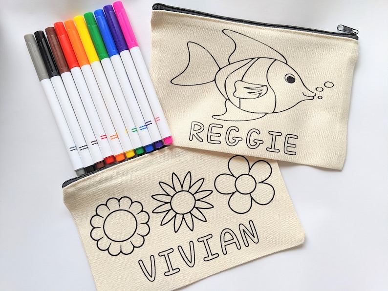 Puede incluir: Dos estuches de cremallera de lona con contornos negros de un pez, flores y los nombres Reggie y Vivian. Los estuches vienen acompa&ntilde;ados de un juego de 12 rotuladores de colores.