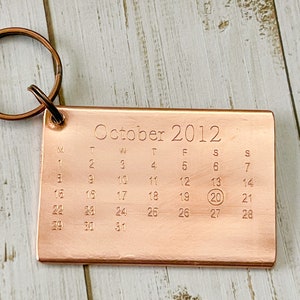 以下が含まれることがあります： 2012年10月のカレンダーが付いた銅製のキーホルダー。カレンダーの20日が丸で囲まれています。