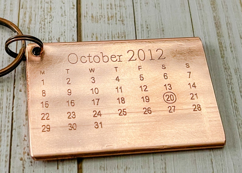 以下が含まれることがあります： 2012年10月のカレンダーが付いた銅製のキーホルダー。カレンダーの20日が丸で囲まれています。