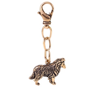 May include: A gold-colored metal keychain featuring a detailed sculpture of a black and brown Collie dog. The keychain has a gold-colored metal chain and a spring-loaded clasp.