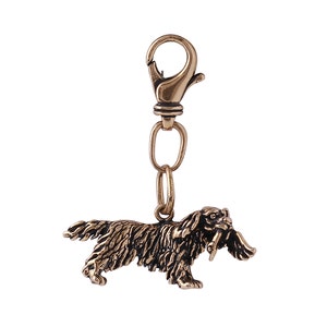 May include: A gold-toned metal keychain featuring a detailed sculpture of a dog holding a bird in its mouth. The keychain has a spring-loaded clasp.