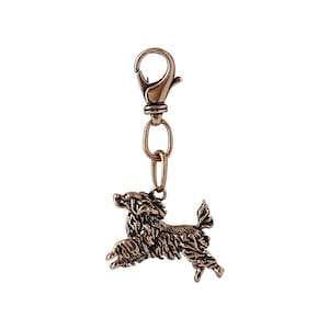 May include: A gold-toned metal keychain featuring a detailed, three-dimensional sculpture of a poodle dog in a jumping pose.