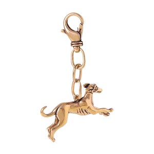 May include: A gold-colored metal keychain featuring a detailed sculpture of a greyhound dog in a leaping pose. The keychain has a metal clasp.