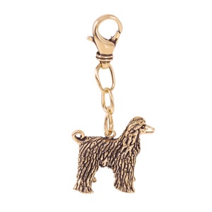 Op de afbeelding: Gouden metalen sleutelhanger met een gedetailleerd gesculpteerd hondje. De hond staat met zijn hoofd naar de zijkant gedraaid en heeft een lange, vloeiende vacht. De sleutelhanger heeft een veerbelaste sluiting.