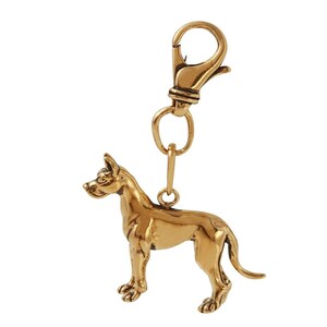 May include: A gold-colored metal keychain featuring a detailed Great Dane dog figurine. The keychain has a spring-loaded clasp.