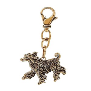 May include: A gold-toned keychain featuring a detailed, three-dimensional sculpture of a black and white dog. The dog is standing on all four paws with its tail curled up. The keychain has a gold-toned metal loop and a spring-loaded clasp.