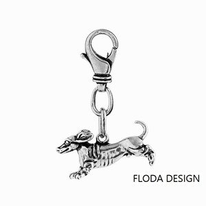 May include: Silver dachshund charm with a spring clasp. The charm is detailed and realistic, with the dachshund in a running pose. The charm is attached to a silver chain.