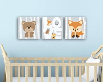 May include: Three framed prints with a woodland theme. The prints feature a bear, a fox, and the word "LOVE" with a bird and a deer. The prints are hanging on a light blue wall above a white cot.