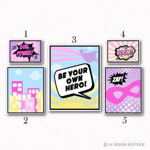 May include: Set of five printable posters with a superhero theme. The posters feature a pink and purple color scheme with illustrations of a superhero flying, a cityscape, a mask, and speech bubbles with the text "Girl Power!", "Be Your Own Hero!", "Boom!" and "Zap!"
