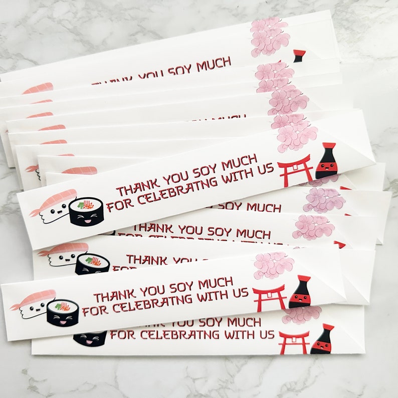 Puede incluir: Una pila de palillos de papel blanco con un dise&ntilde;o de sushi rojo y negro y el texto "Thank you soy much for celebrating with us".