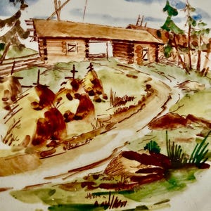 May include: A decorative plate featuring a hand-painted landscape scene. The artwork depicts a log cabin with a brown roof, set against a backdrop of green trees, a winding path, and a blue sky with clouds. The plate's rim is white.
