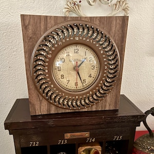 May include: An antique clock with a brown wooden frame and a circular, bronze-coloured face. The clock face features Roman numerals and the brand name "Remington". The clock is set on a dark wooden cabinet.