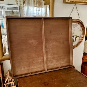 May include: An open, wooden box with a hinged lid. The box is made of light brown wood and has a rectangular shape. The lid is open, revealing the interior of the box. The box is sitting on top of a larger wooden surface.