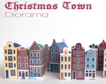 Puede incluir: Un diorama de papel de una ciudad navideña con casas coloridas. El título "Christmas Town Diorama" está en la parte superior de la imagen. El texto "Without the numbers" y "Sans numéros" está en la parte inferior de la imagen.