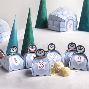 May include: A papercraft Christmas village featuring penguins, igloos, and trees. The penguins are numbered 1 to 23, and the igloos are numbered 5 and 22. The text "THE PEGUINS CHRISTMAS VILLAGE" is at the top of the image. The text "Copyright 2015 PapierBonbon - All rights reserved. For personal use only http://PapierBonbon.etsy.com" is at the bottom of the image.