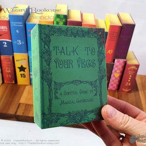 May include: A green book with the title "TALK TO YOUR VEGS" and the subtitle "A Survival Guide to Magical Gardening". The book is part of a set of miniature books that are arranged in a bookcase.