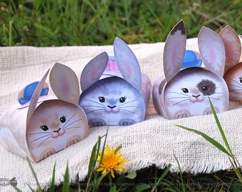 Puede incluir: Cuatro adorables cajas con forma de conejo con sombreros azules. Las cajas están hechas de papel y están decoradas con ilustraciones de acuarela de conejos. Las cajas son perfectas para guardar pequeños regalos o golosinas.